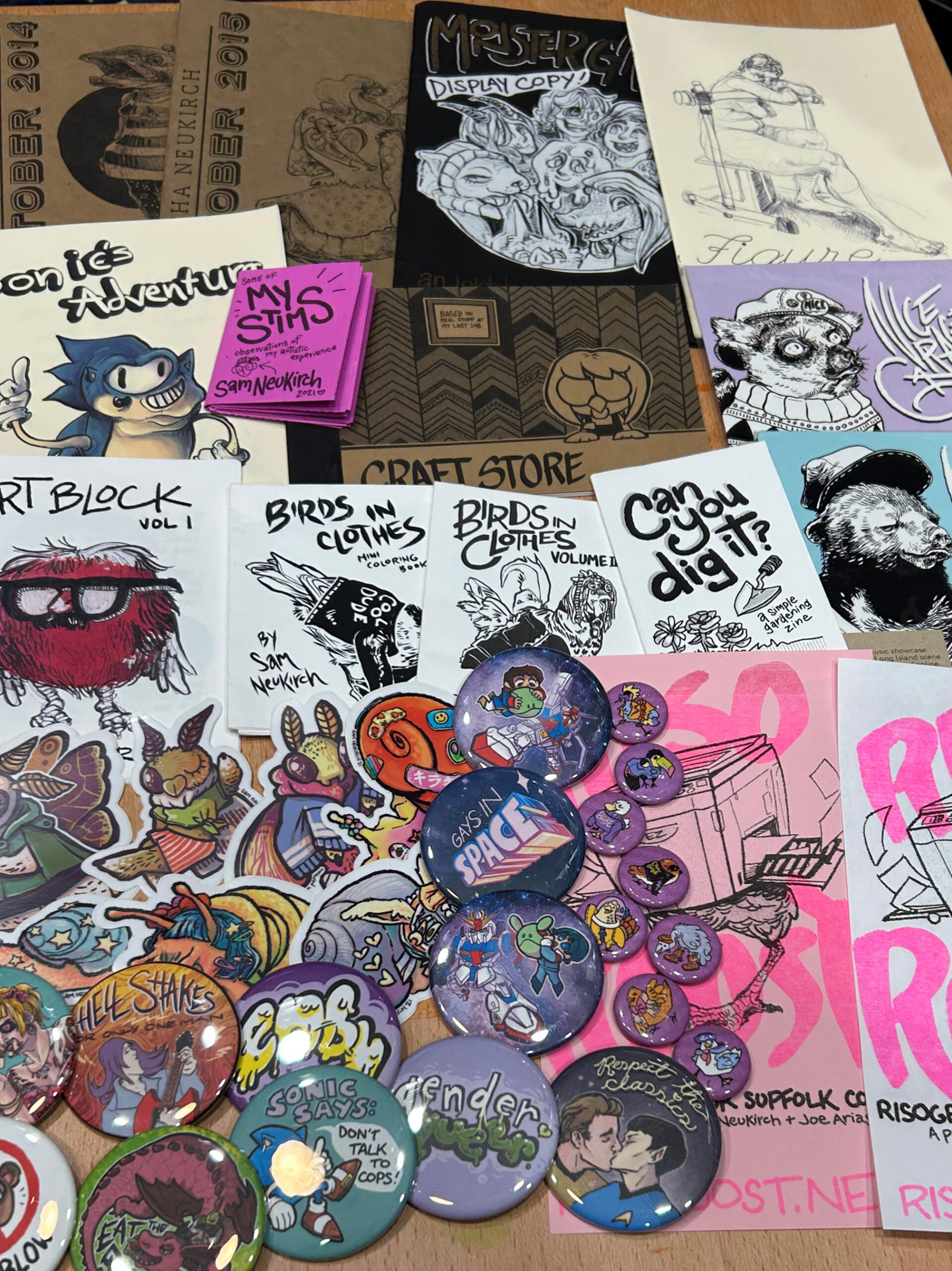 A photo of much of the merch Sam has made for selling, including a bunch of art zines, vinyl stickers of snails and moths, and a bunch of pinback buttons.